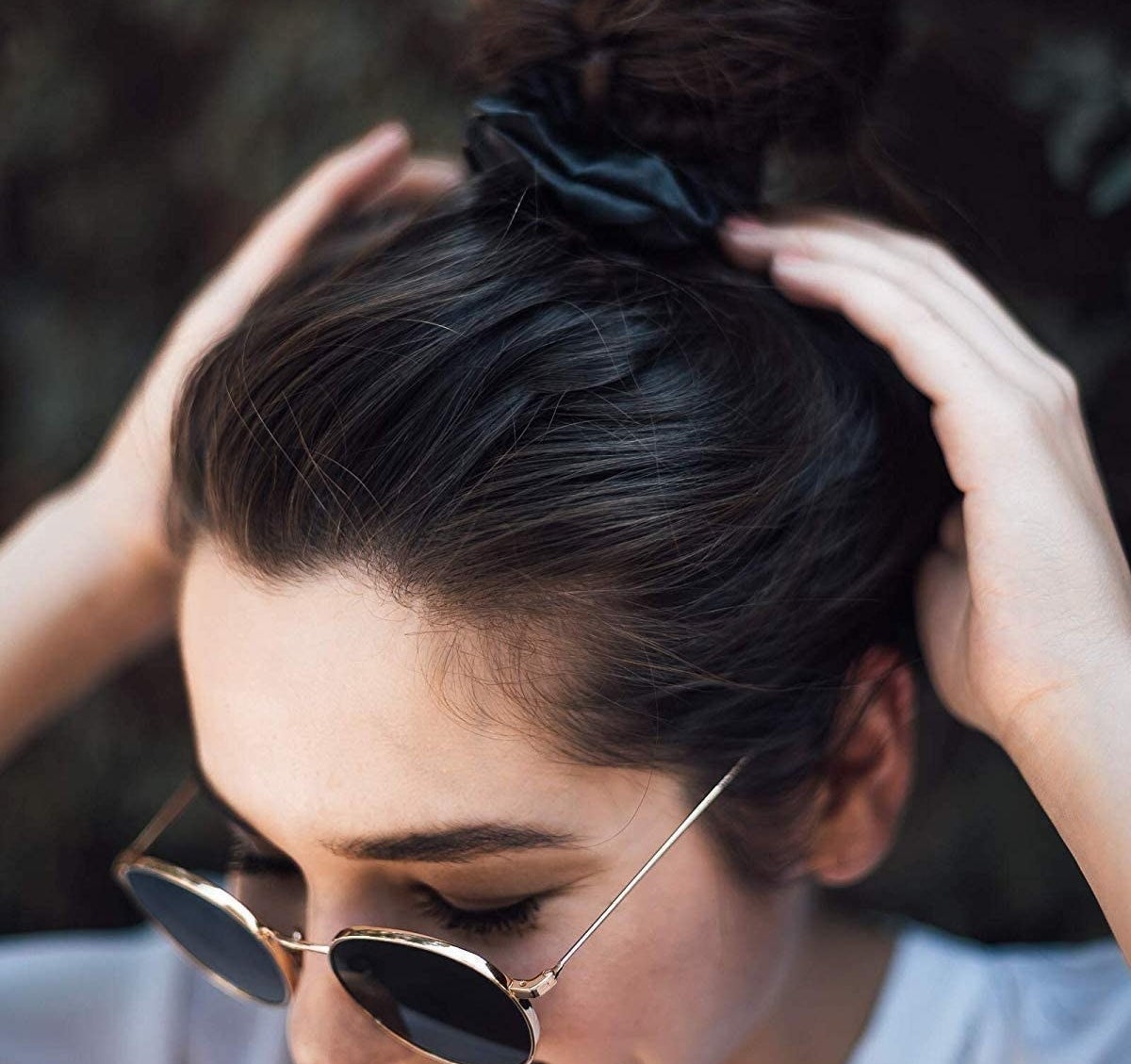 A person wearing sunglasses and a silk scrunchie in their hair
