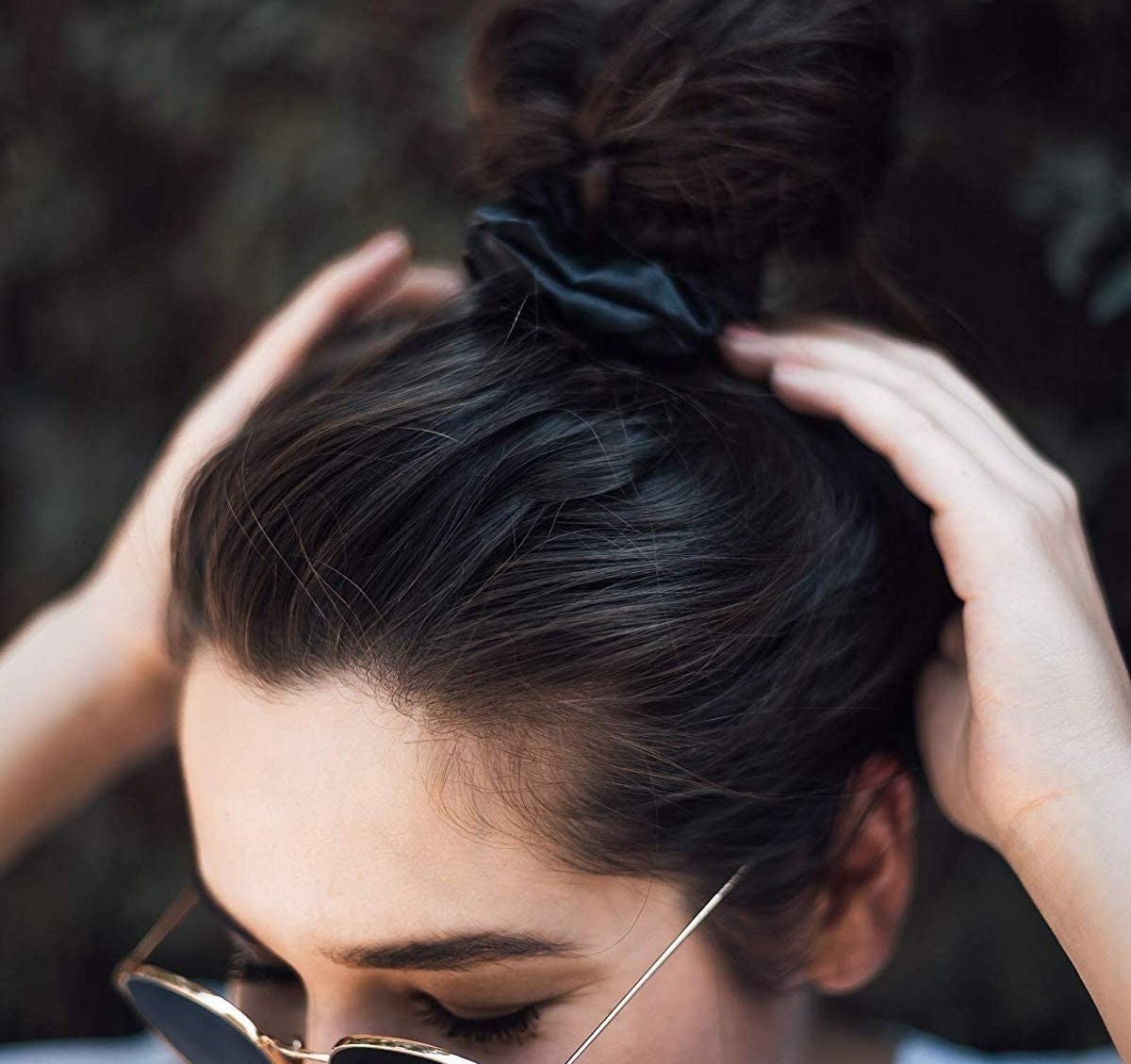 A person wearing sunglasses and a silk scrunchie in their hair