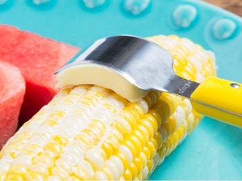 The curved butter knife gliding a slide of butter along a cob of corn 