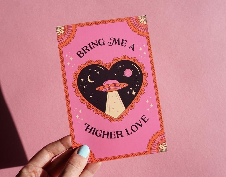 A pink card with a drawing of a heart with a spaceship inside it, and the words "Bring me a higher love" outside the heart