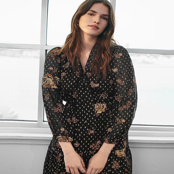Close up of a model wearing the 3/4-sleeve v-neck dress in black with gold and brown pattern to it