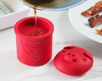 Oil being poured strained into the red silicon bacon pin sitting next to the matching silicone lid shaped like a pig's head 