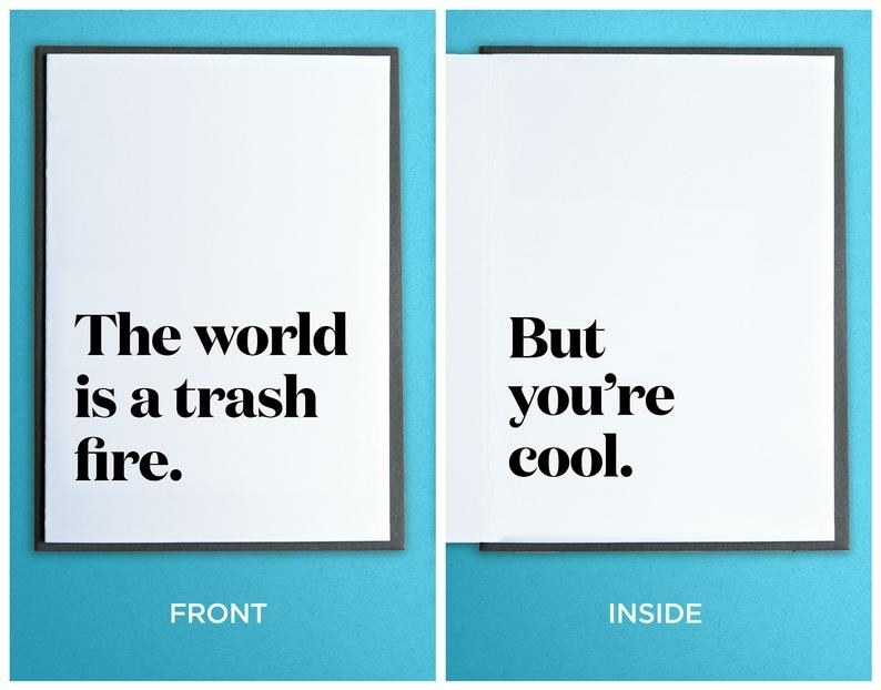 A white card with black text on front: "The world is a trash fire" and inside: "But you're cool."