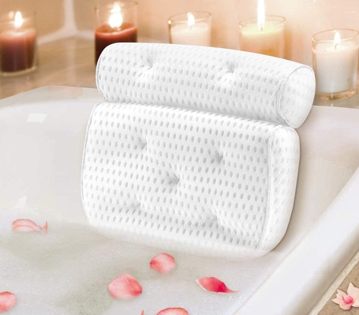 A bathtub pillow with neck and back support in a tub surrounded by flower petals and candles 