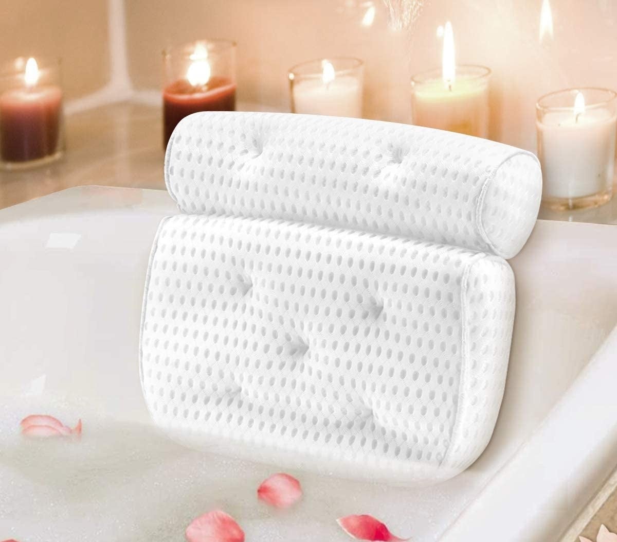 A bathtub pillow with neck and back support in a tub surrounded by flower petals and candles