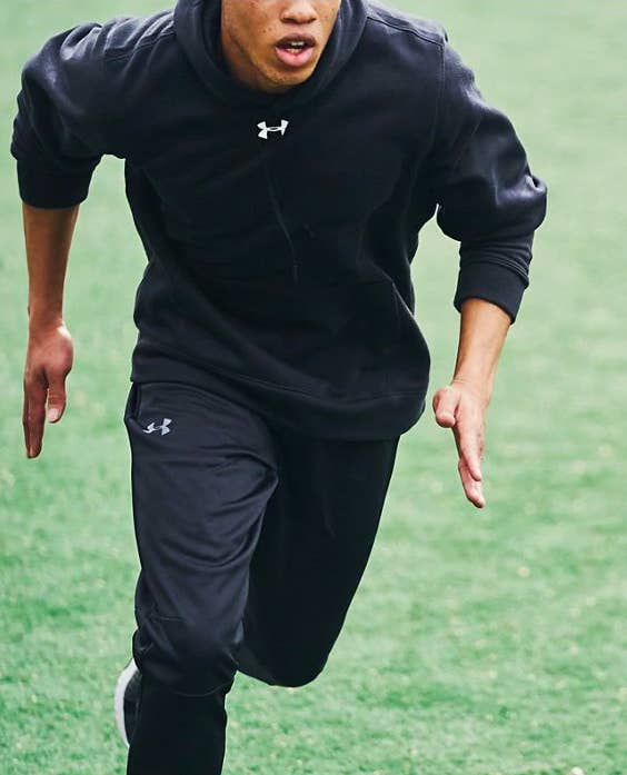 a model wearing the hoodie in black and running on a field 