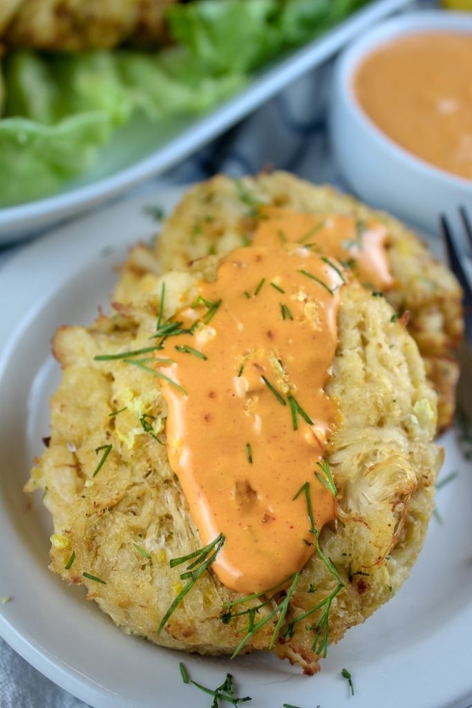 A plate of air fried crab cakes topped with herbs and spicy sauce.