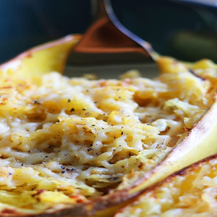 A fork pulling the cheesy interior out of a halved spaghetti squash.