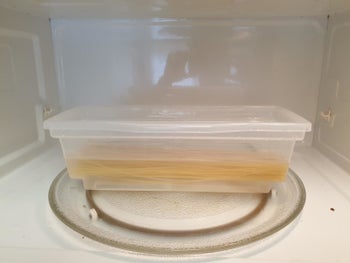 A reviewer photo of uncooked pasta and water in the clear, plastic microwave pasta cooker 