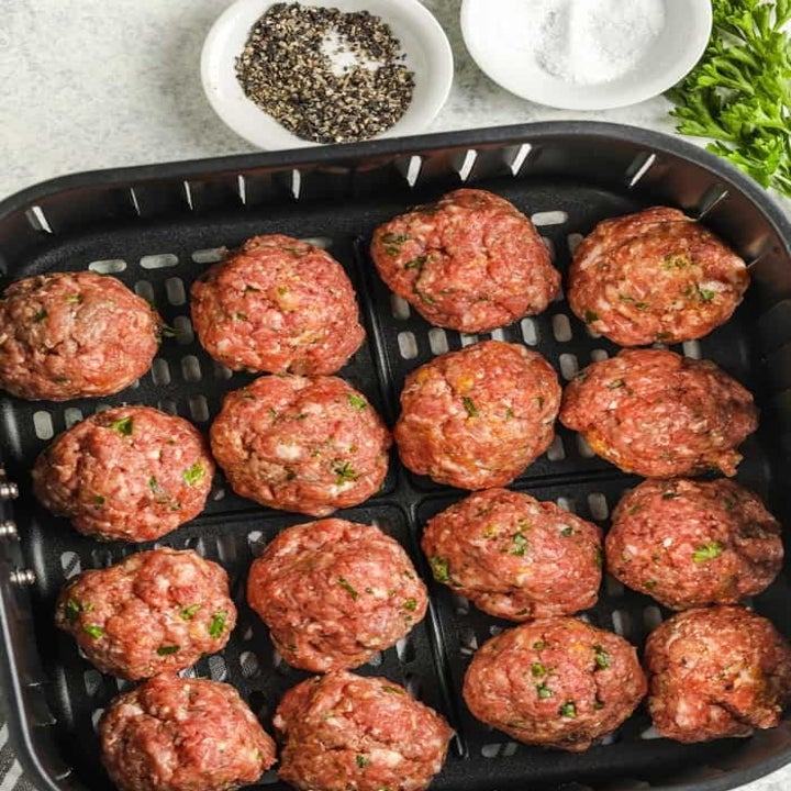 Uncooked meatballs in the basket of an air fryer.