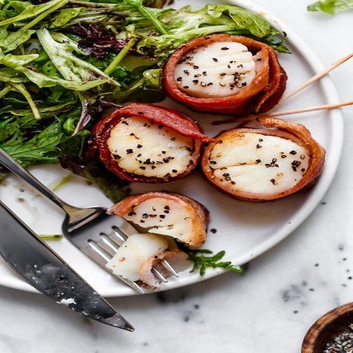 A plate of scallops wrapped in crispy bacon with arugula on the side.