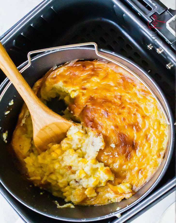 A creamy corn casserole with a crispy top layer in the basket of an air fryer.