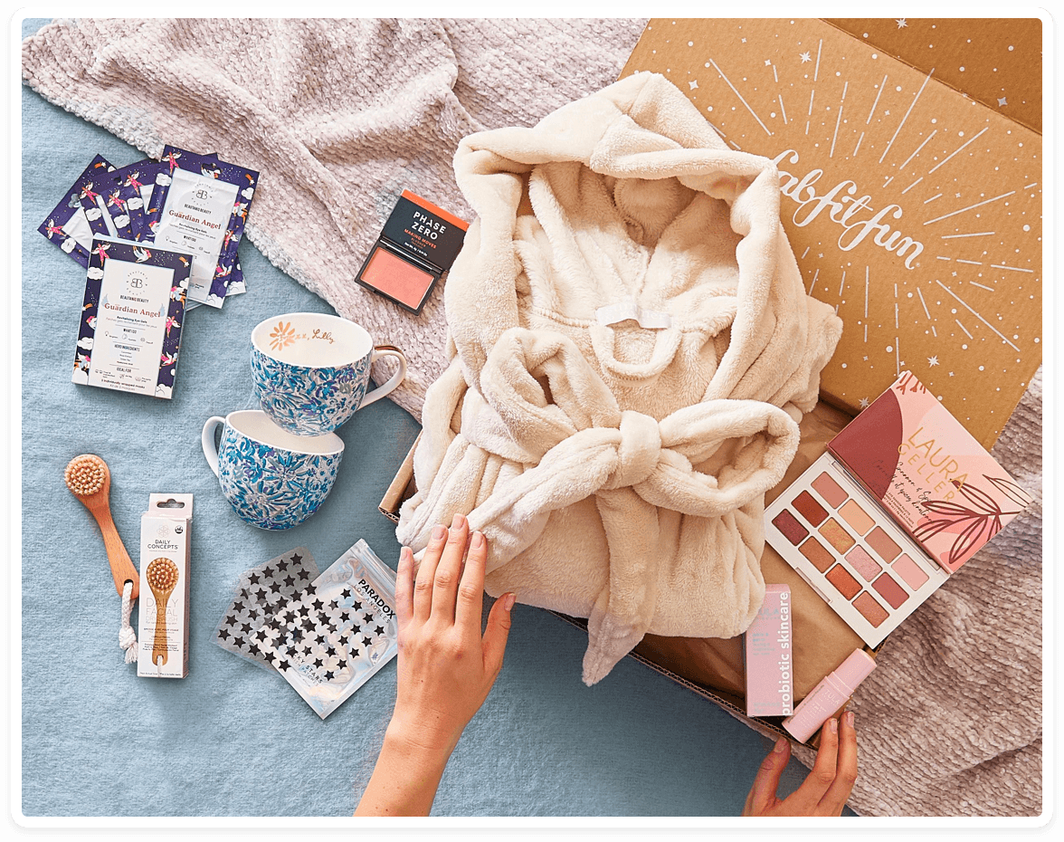 A box and its contents laid out, including a robe, eyeshadow, mugs, pimple stickers, a body brush, and more