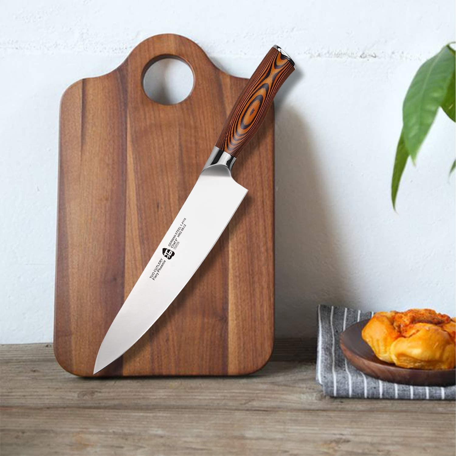 A large stainless steel chef&#x27;s knife with a pakkawood handle on a wooden countertop