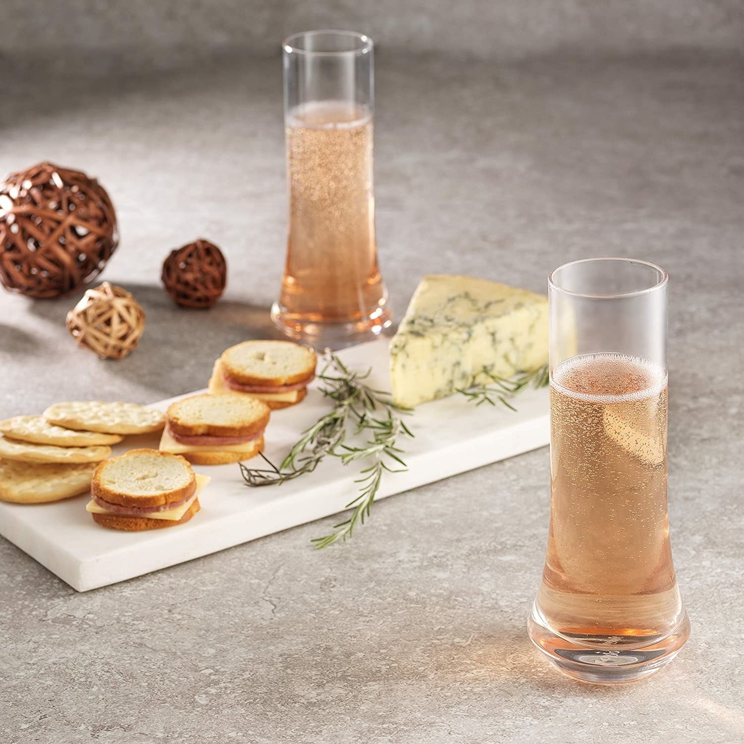 A pair of stemless flutes filled with champagne next to an elegant cheeseboard