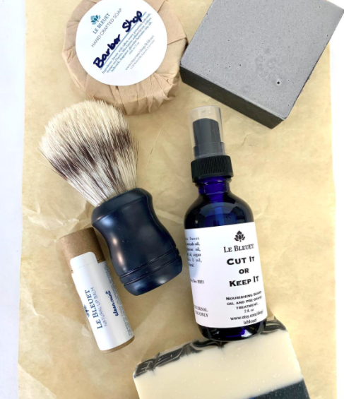 A flatlay of the grooming set to show the soap, shaving brush, beard oil, lip balm, and barber&#x27;s soap