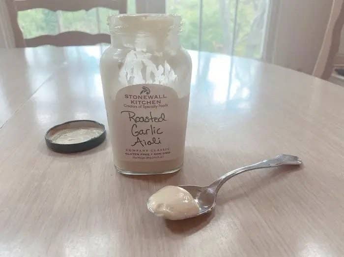 a spoon filled with the roasted garlic condiment next to an open jar