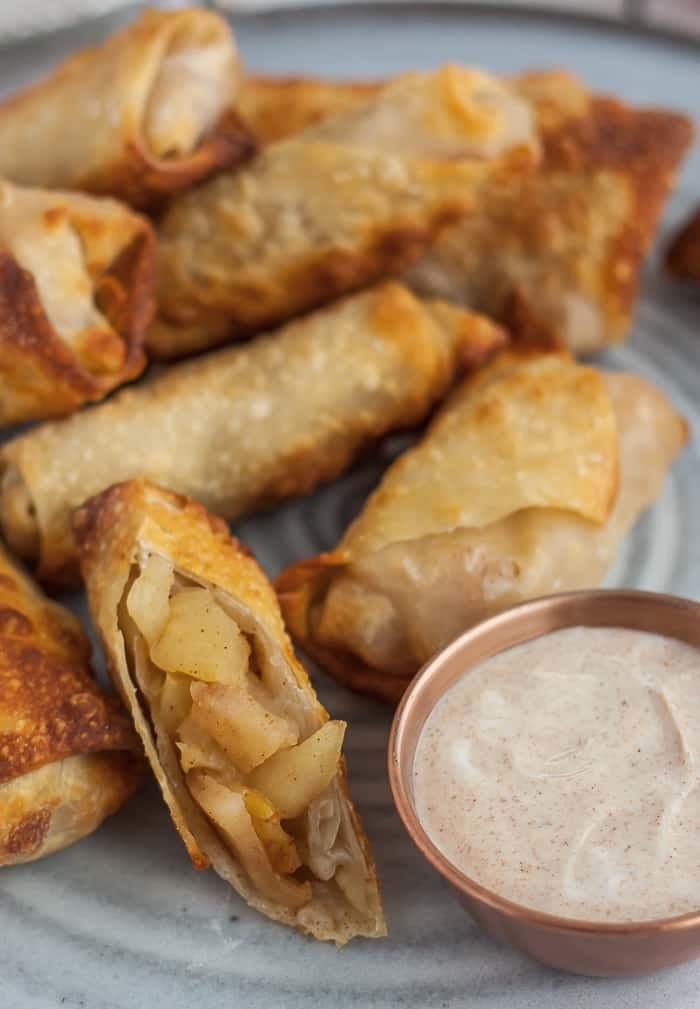 A plate of apple pie egg rolls with cinnamon, creamy dipping sauce.