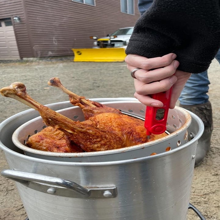A reviewer photo of a hand sticking the meat thermometer into a turkey cooking in a deep fryer 