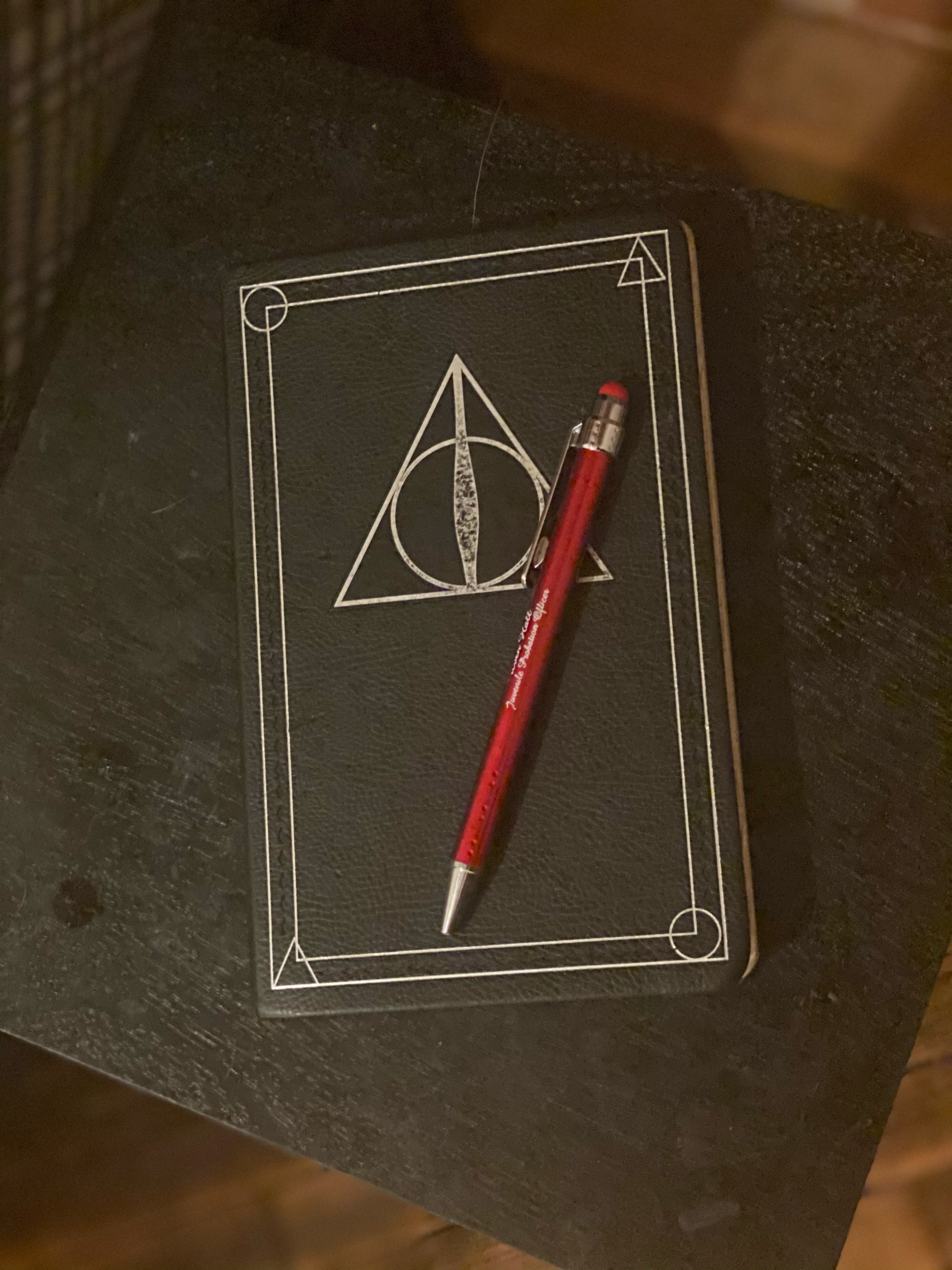 A red pen sit on top of a black Harry Potter themed notebook. 