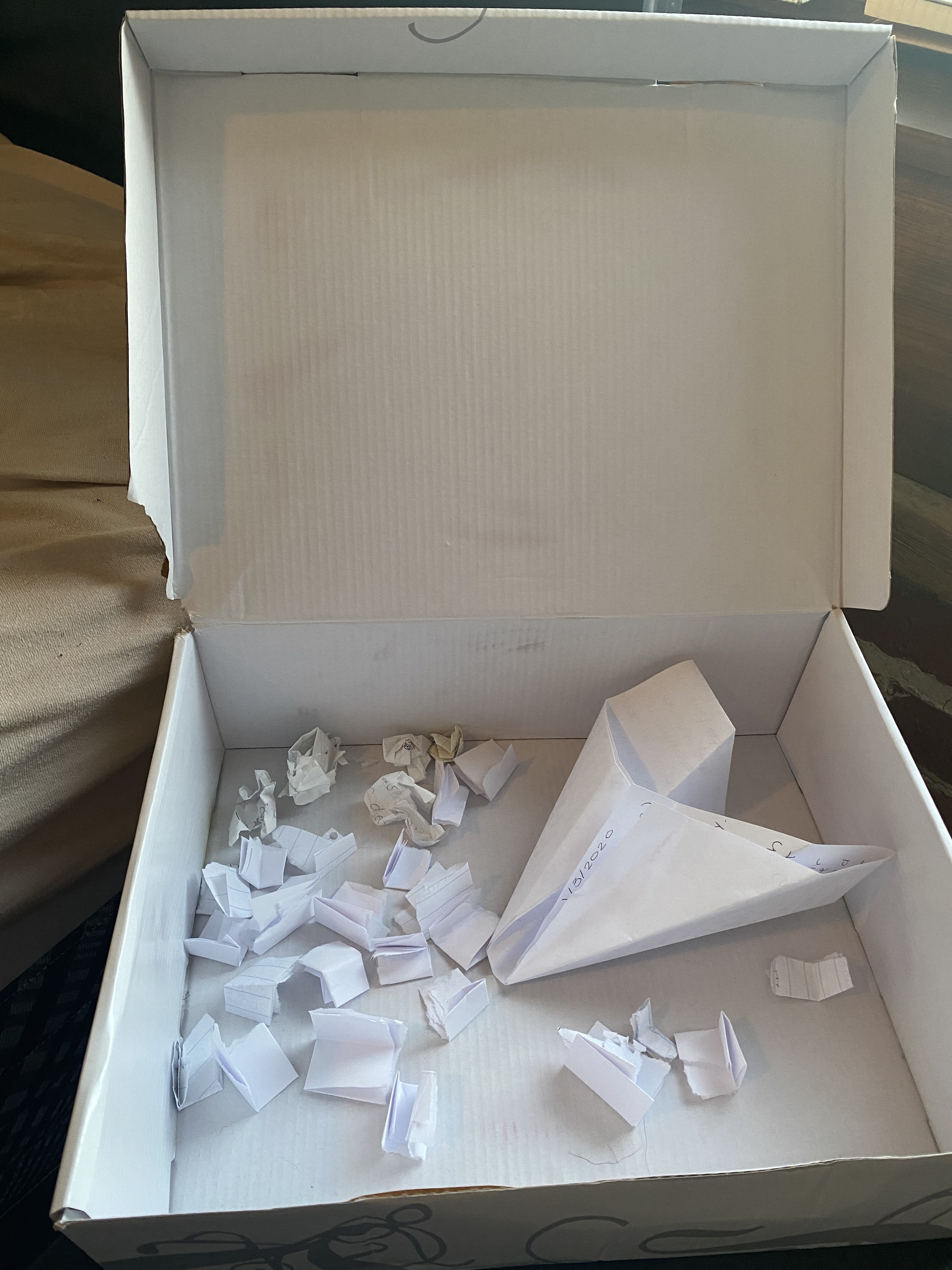 A white shoebox is filled with multiple pieces of folded up paper. 