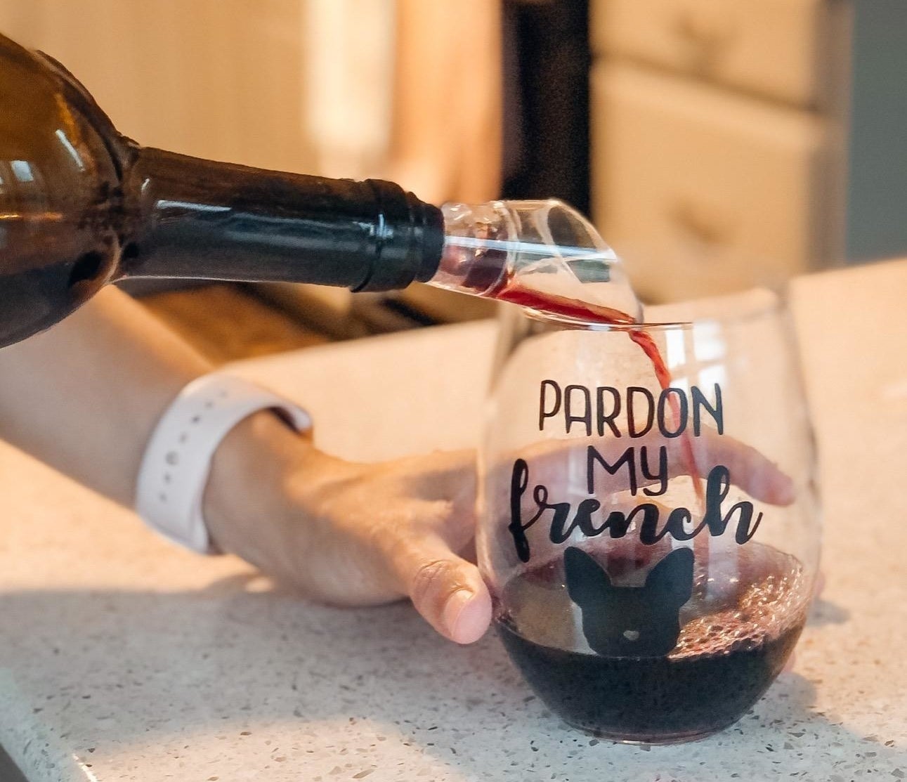 A reviewer photo of a hand pouring a bottle of wine with an aerator stuck in the top into a wine glass that says "Pardon my french" with an image of a French Bulldog head
