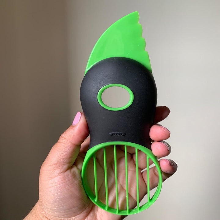 A handle holding the green and black avocado slicer with a serrated blade at the top, a round pit remover in the middle, and a fan blade to cut the avocado into seven pieces 