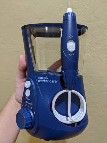 A reviewer's photo of the blue Waterpik which has a dial and three buttons