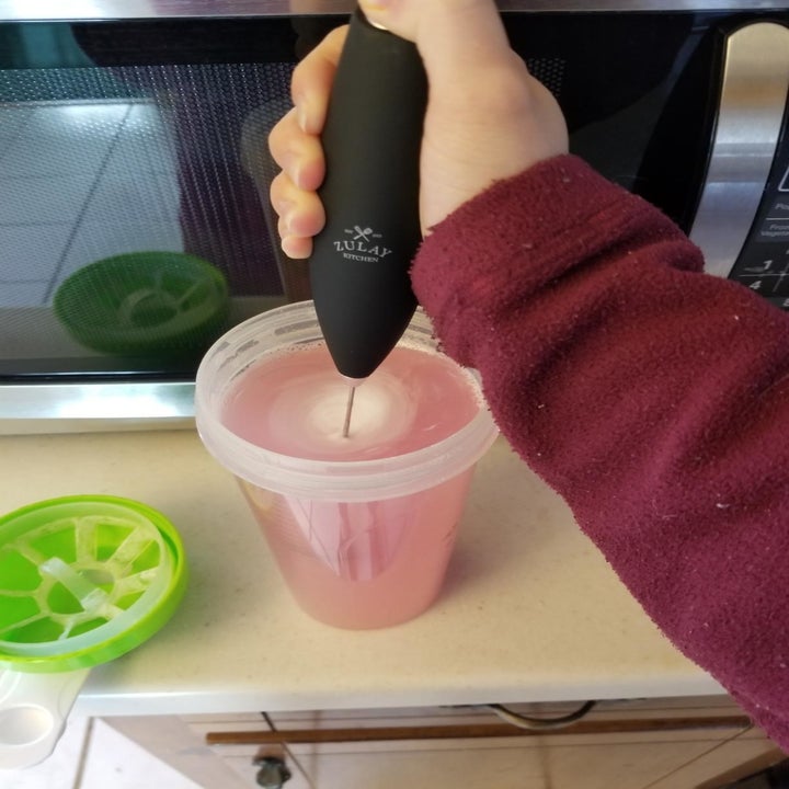 A reviewer photo of a hand using the milk frother to blend supplements into a pink beverage 
