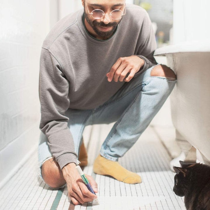 a man squatting down to use the grout pen on the bathroom floor