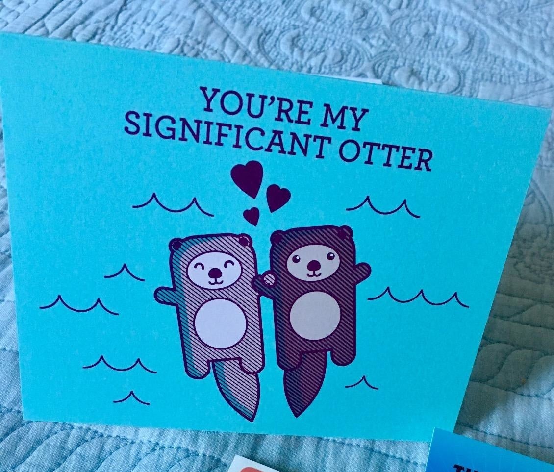 A blue card with a drawing of two otters holding hands in the sea and "You're my significant otter" in black type