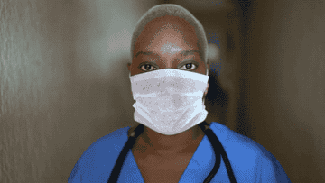 A frontline worker in a face covering looks into camera 