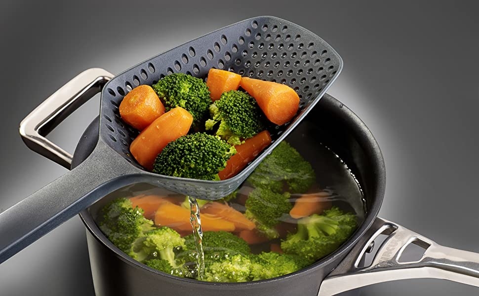 A spoon with drainage holes scooping vegetables out of a pot full of water and vegetables 