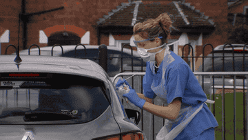 A frontline worker performs a COVID test to a patient inside a car 