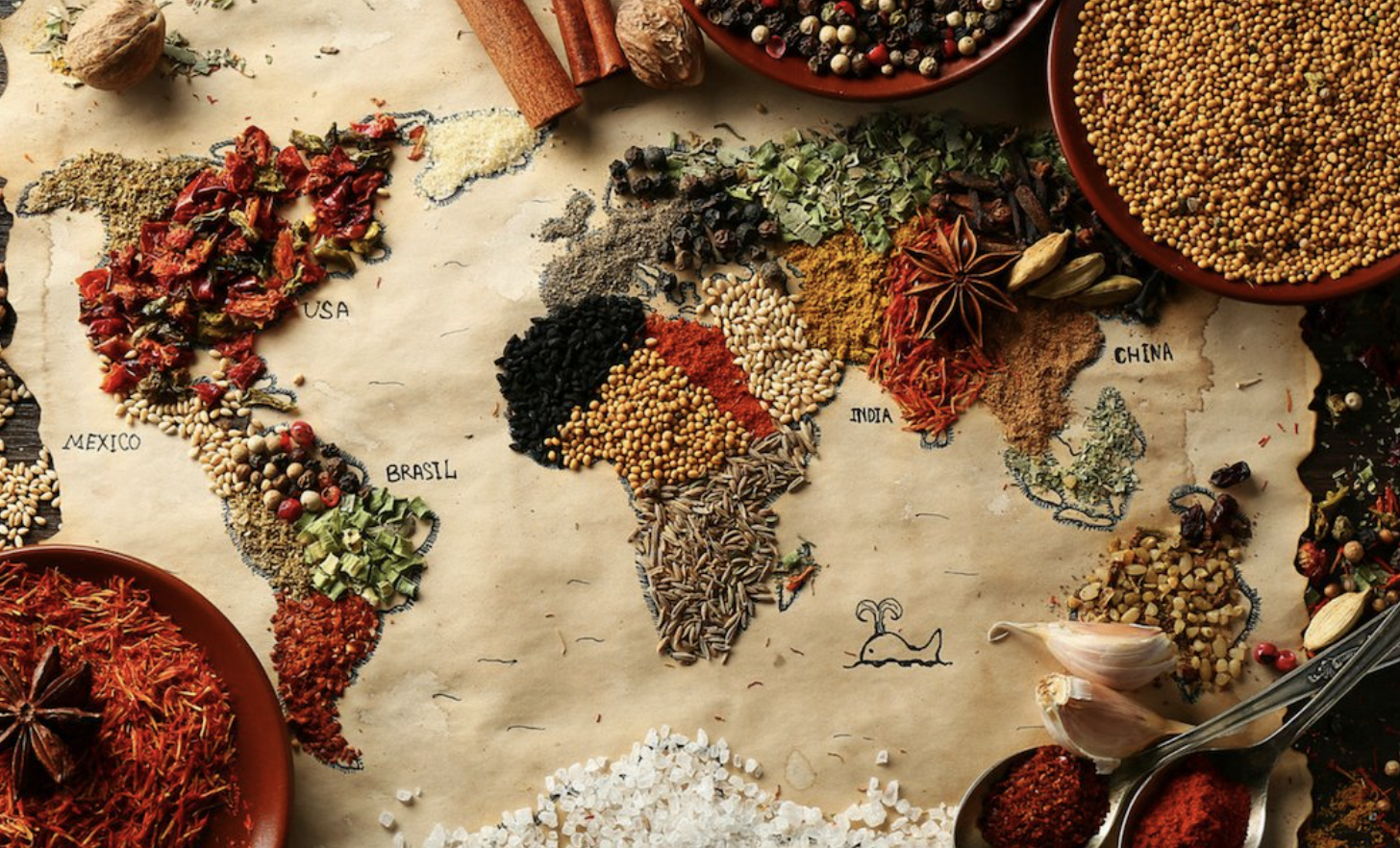 A variety of colorful spices in the shape of a global map across brown paper, with bowls of spices surrounding