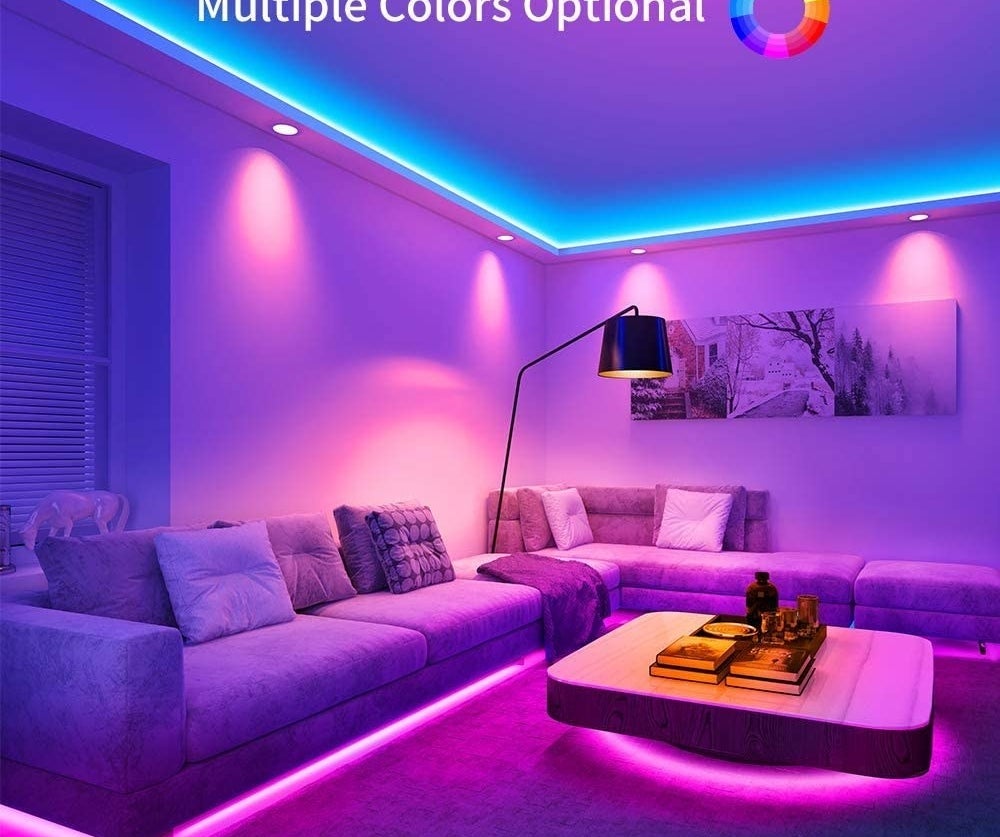 A living room with long couches lined with the LED light strips below them on the floor, and above along the ceiling 