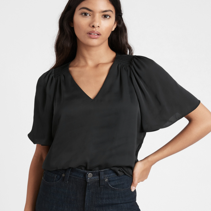 Model wearing satin flutter-sleeve top in the shade black