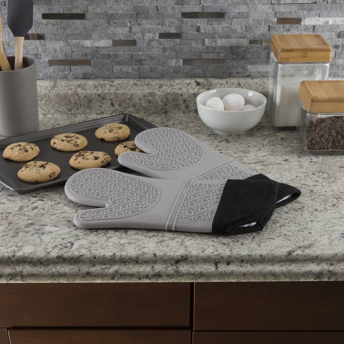 two grey silicon oven mitts next to a tray of cookies on counter