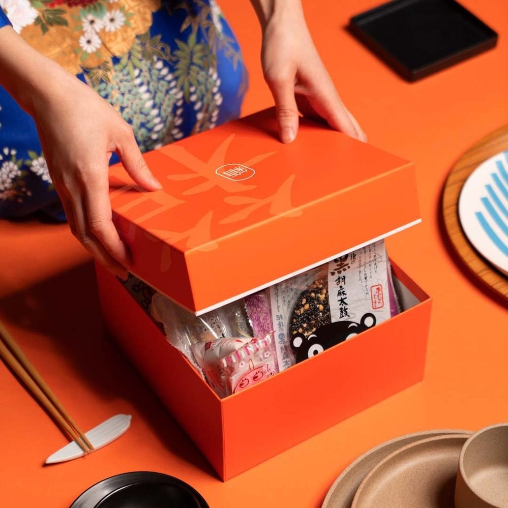 Hands opening an orange box with Japanese foods inside