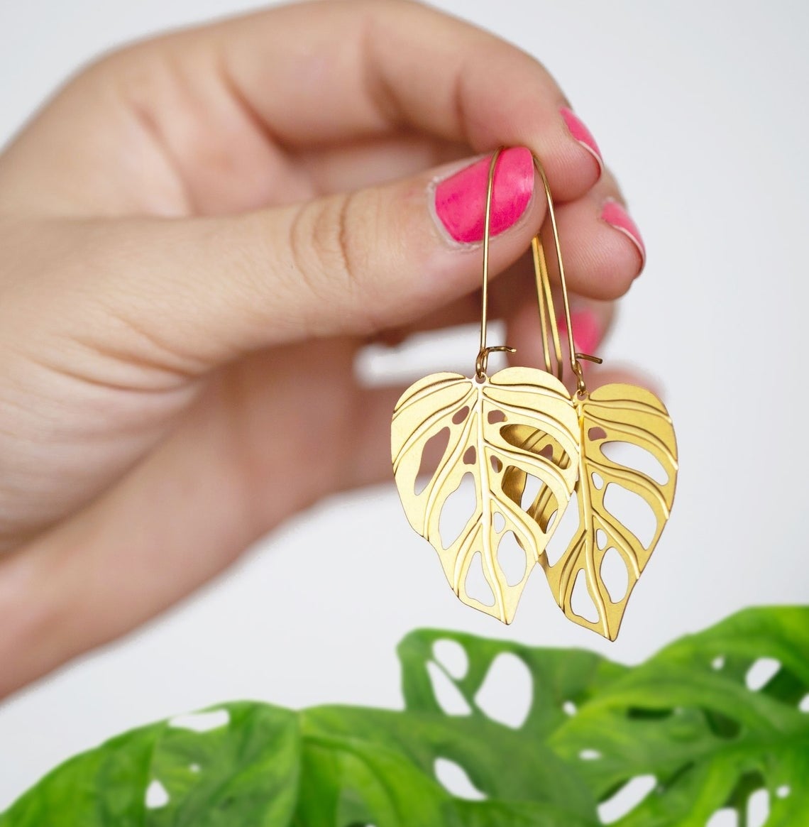 A person holding the monstera earrings above a plant