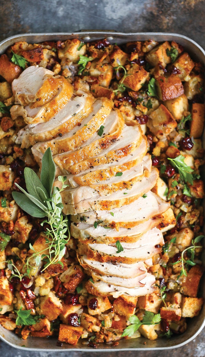 A baking dish of cranberry pecan herb stuffing with a sliced turkey breast on top.