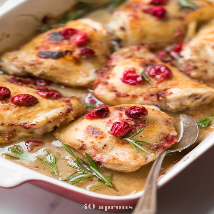 Chicken thighs in a cream sauce topped with cranberries in a baking dish.