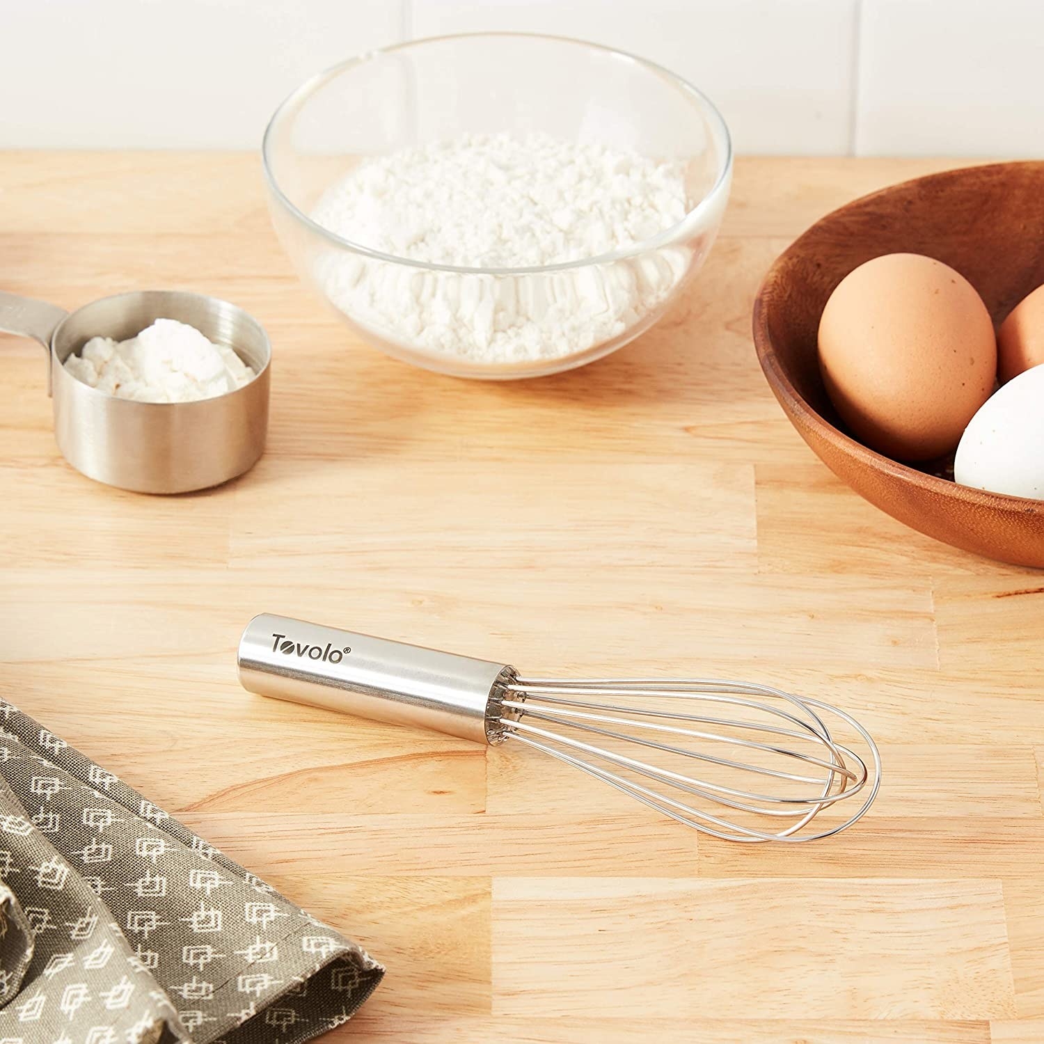 the whisk on a table surrounded by flour and eggs