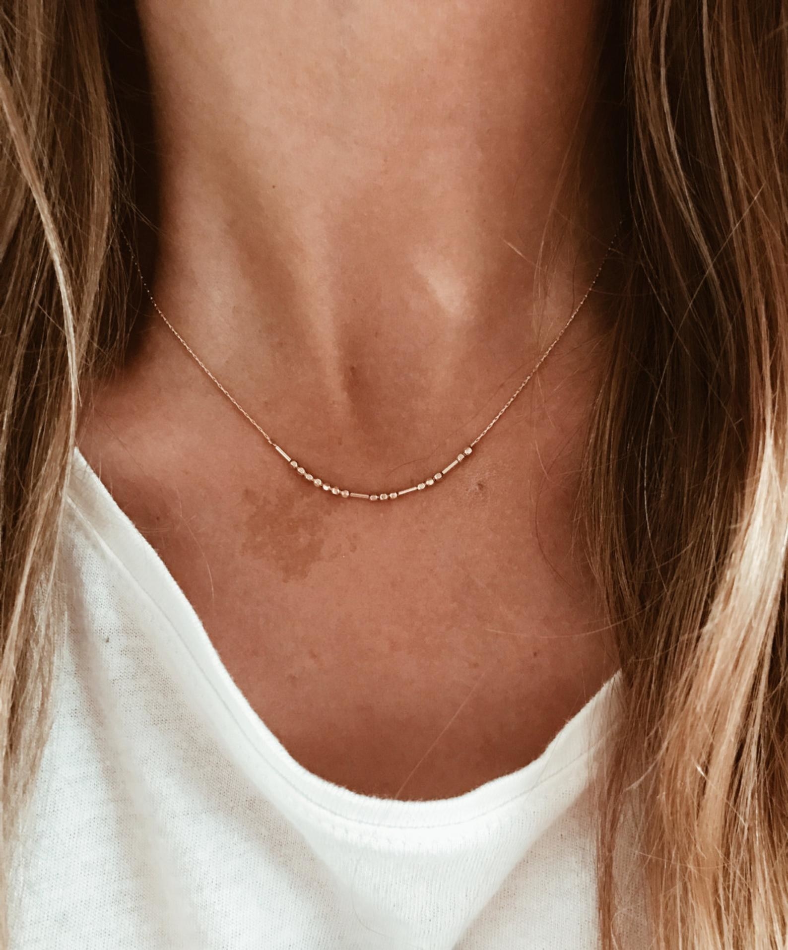 a person wearing the morse code necklace in gold 