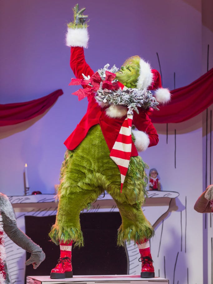 Matthew Morrison in his Grinch costume posing on a table with one arm up and the other on his hip.