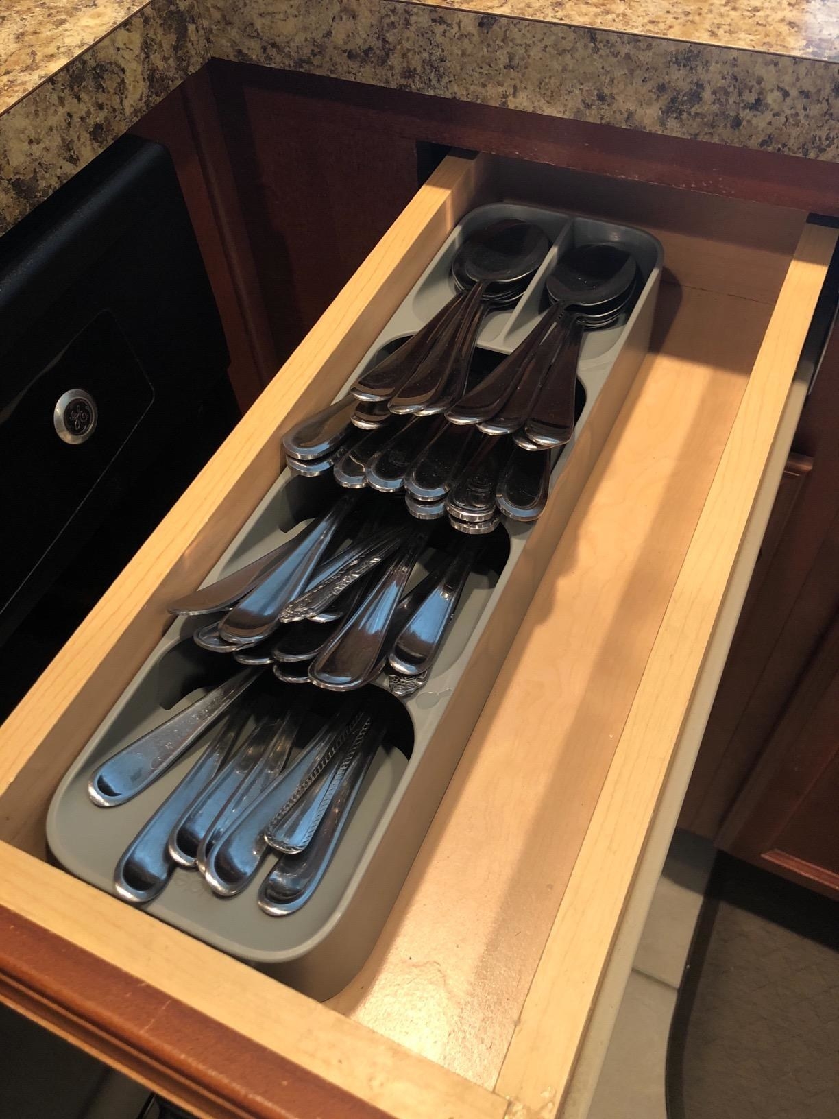 A reviewer&#x27;s photo of the cutlery organizer placed in a small kitchen drawer
