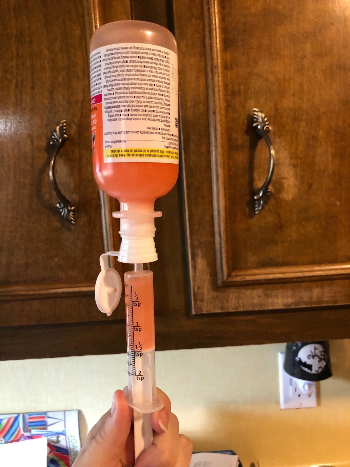 Reviewer&#x27;s photo of them using the syringe with pink medicine