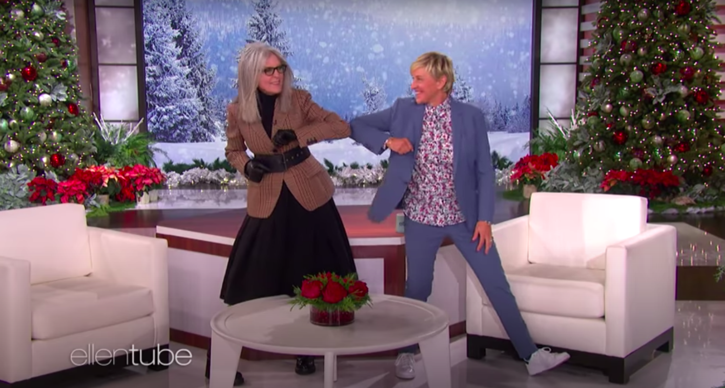 Diane Keaton, wearing a jacket and black gloves, dances with a smiling Ellen DeGeneres, dressed in a blue blazer and floral shirt, as the TV show&#x27;s set is decorated with Christmas trees