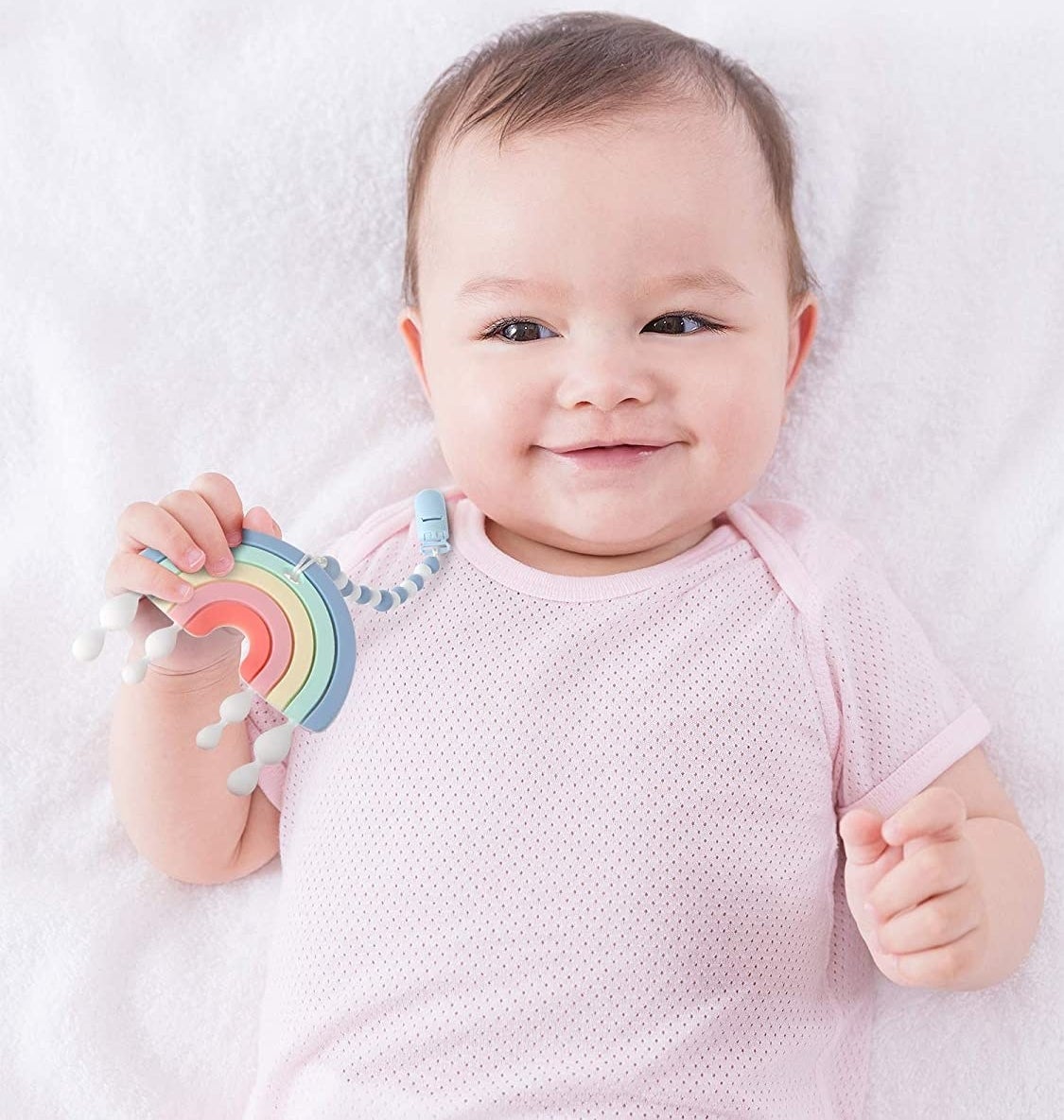 a baby with a rainbow teether clipped to their shirt