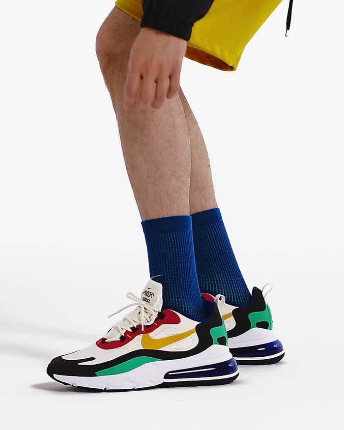 Model wears white Nike Air Max 270s with red, green, and navy blue detailing and dark blue compression socks